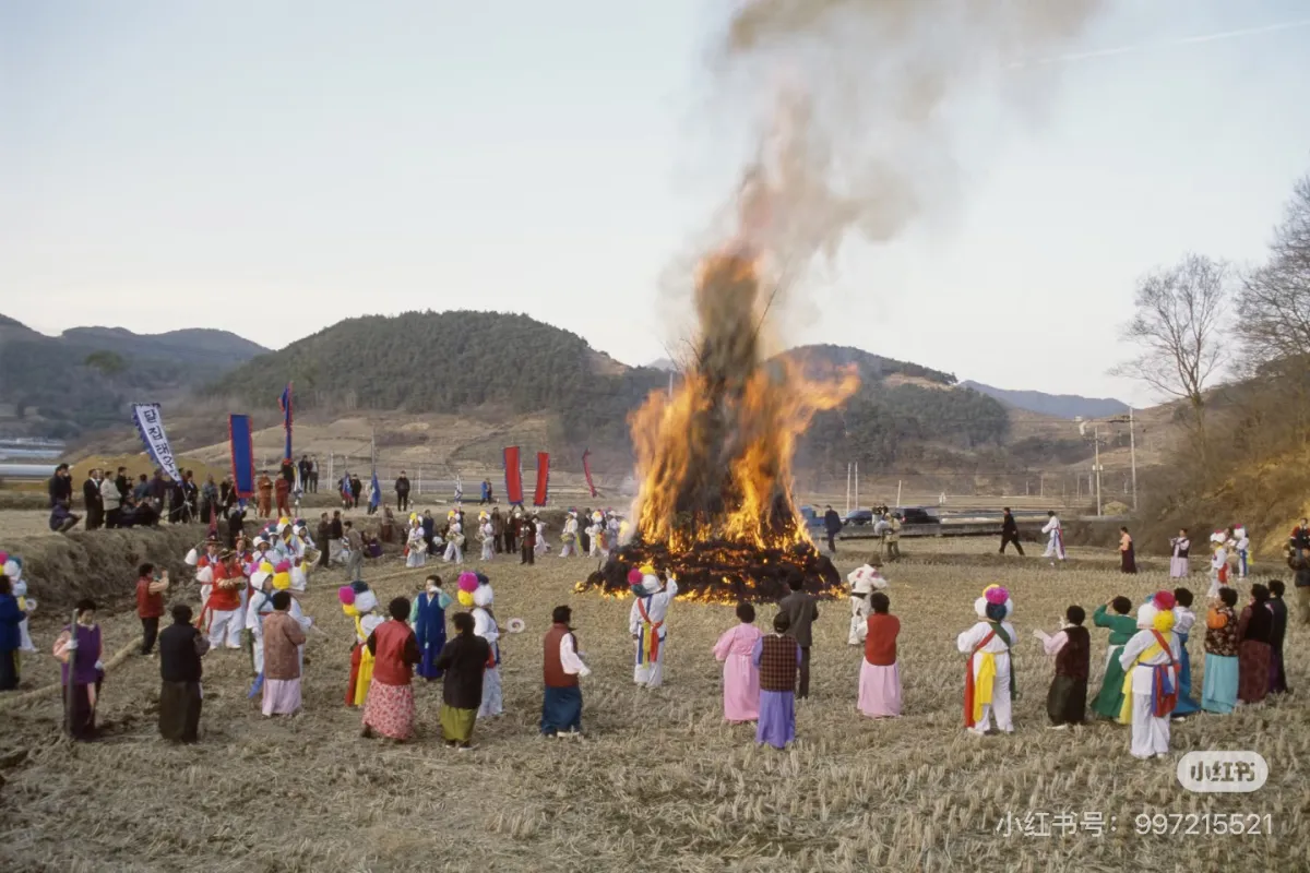 Daljip Taeugui bonfire ceremony during Jeongwol Daeboreum — community gathered around a large straw fire in traditional Korean dress
