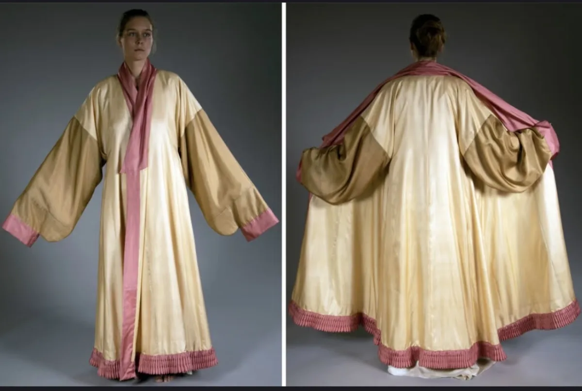 Reconstruction of a Han-dynasty silk robe from the Niya archaeological site, showing cream-gold silk with pink trim, cross-collar cut, and wide sleeves